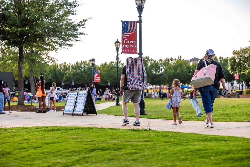 People with bags and chairs walk down sidewalk into park