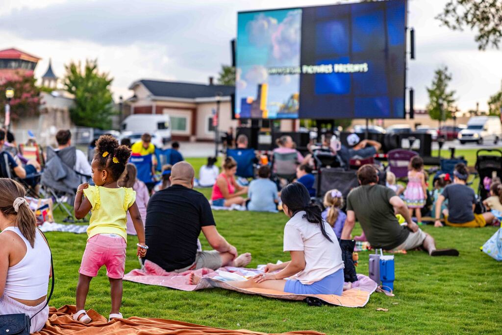 Image shows families sitting on blankets in Greer City Park watching a portable movie screen