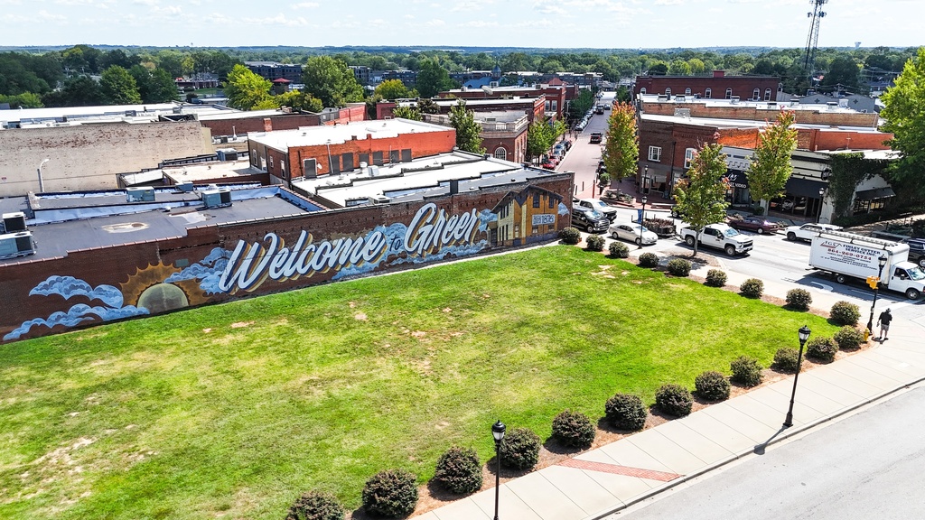 Welcome to Greer, clouds, sun, and the Historic Greer Depot painted in a mural on the side of The Great Bay Oyster House, a brick building at the corner of Main and Poinsett Streets