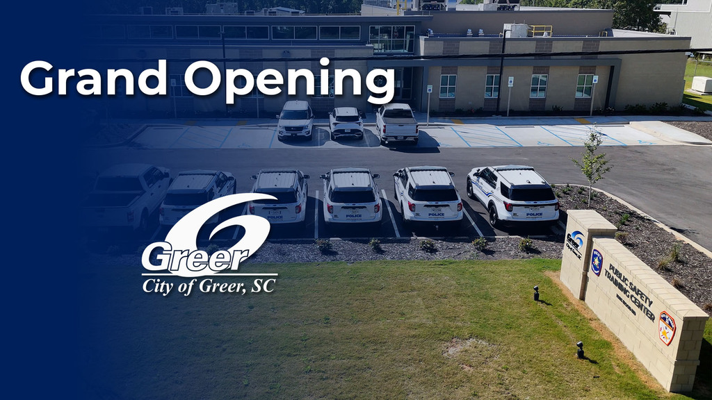 Text says Grand Opening over an aerial shot outside the new Public Safety Training Center, which is a brown brick building; the City of Greer logo is superimposed over the picture
