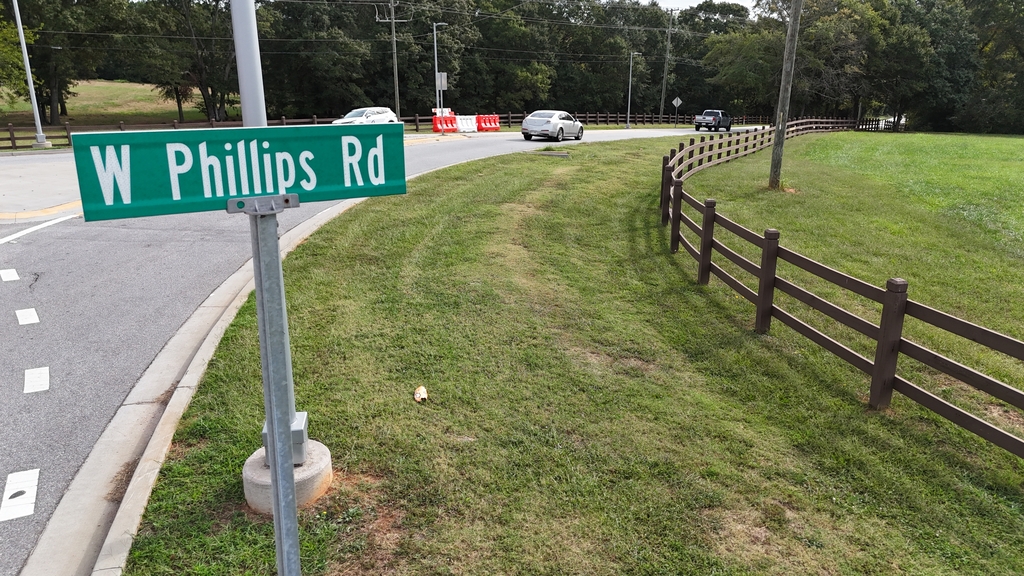 Sign says W Phillips Rd. It's on the side of the street next to a large property surrounded by a brown fence.