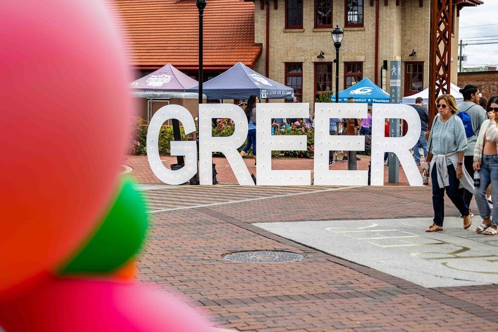 Balloons on left side, large lighted letters that spell out Greer in the center, and festival goers on right
