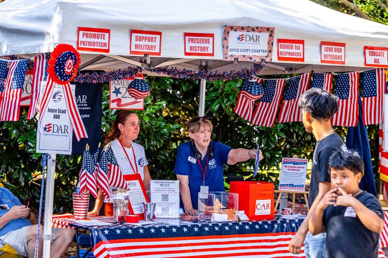 Two women hand out flyers under tent