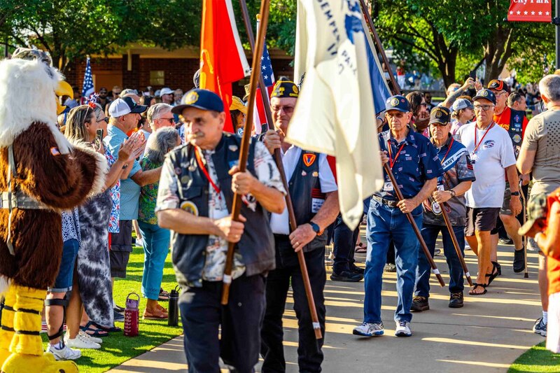 Military veterans walk with flags while crowd watches on and cheers