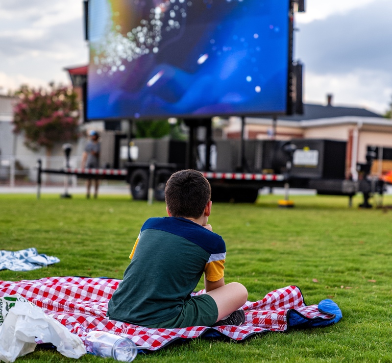 Child sitting on a red and white checkered blanket looking at the screen for Moonlight Movies
