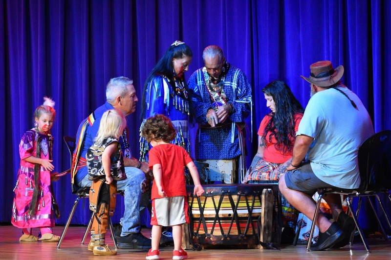Picture shows adults and children on a stage surrounding a large drum