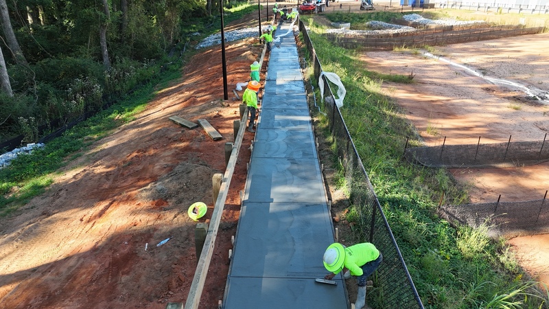 men in safety gear smoothing out concrete of a walking path with trowels