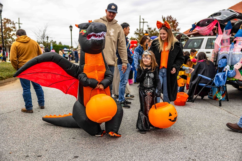Family with a dad, mom, and two kids; one is dressed up as a dragon and the other as a skeleton; they are carrying pumpkin buckets to collect candy