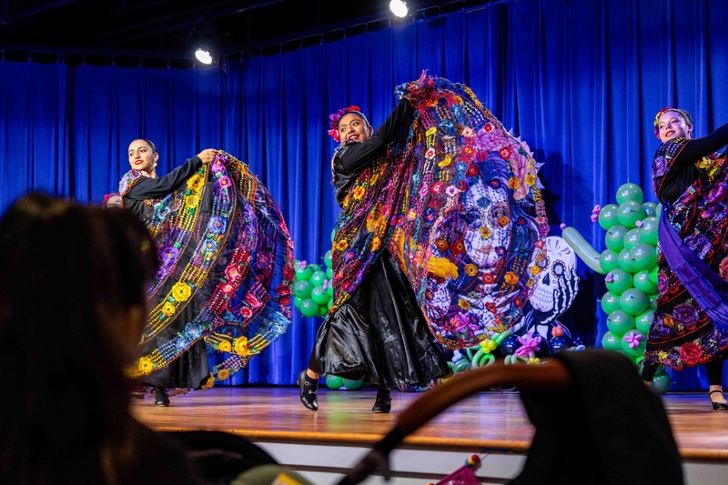 group of young ladies in colorful dresses dancing on a stage with a blue curtain in the background