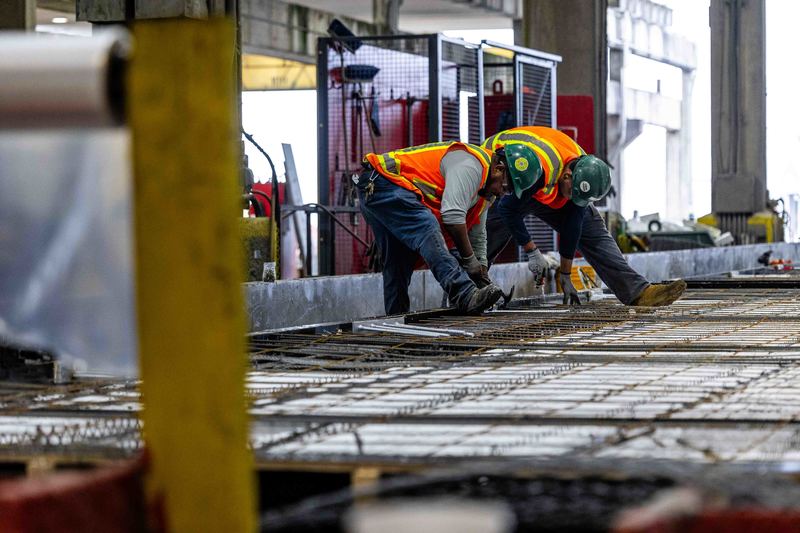 Two workers in safety gear work on rebar assembly of massive pre-cast concrete wall
