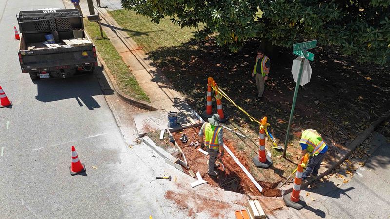 Drone shot of three men digging up sidewalk on street corner
