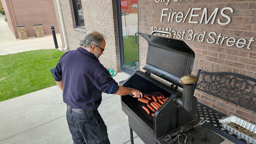 man cooking hot dogs on a grill