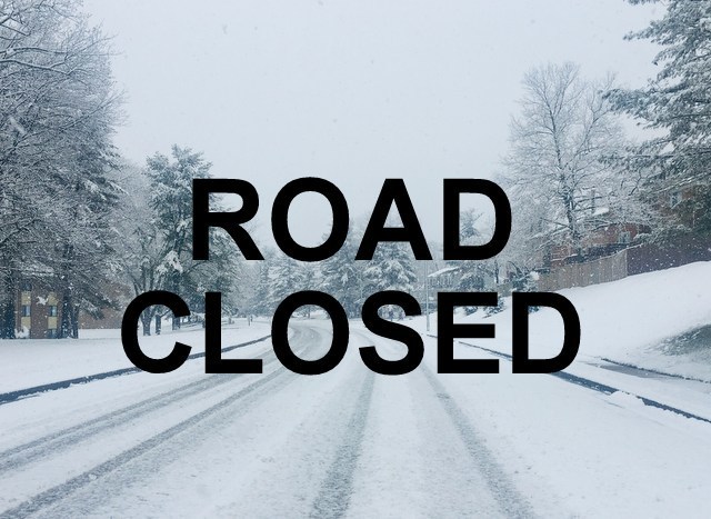 White snow covered road with tire tracks with an overlay of large black capital letters that state “Road Closed”