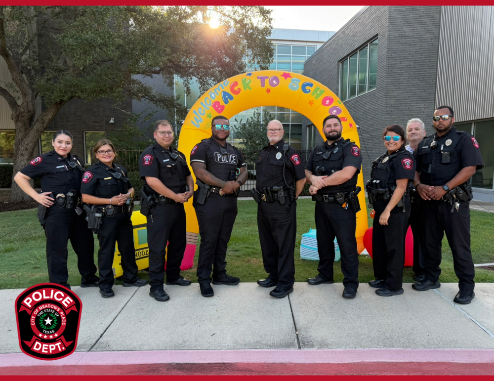 Group of Meadows Place Police Department officers standing outside a school in front of a colorful “Welcome Back to School” arch. The officers are gathered on the first day of school, with the Meadows Place Police Department logo displayed in the lower left corner.