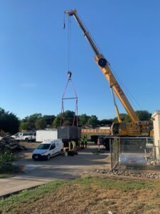 Large yellow crane hoisting a new industrial generator into place at a wastewater treatment plant