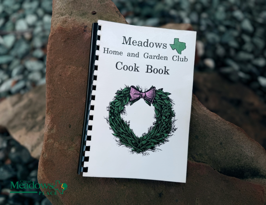 Meadows Home and Garden Club cookbook displayed on a rock, featuring a green wreath and pink bow on the cover.