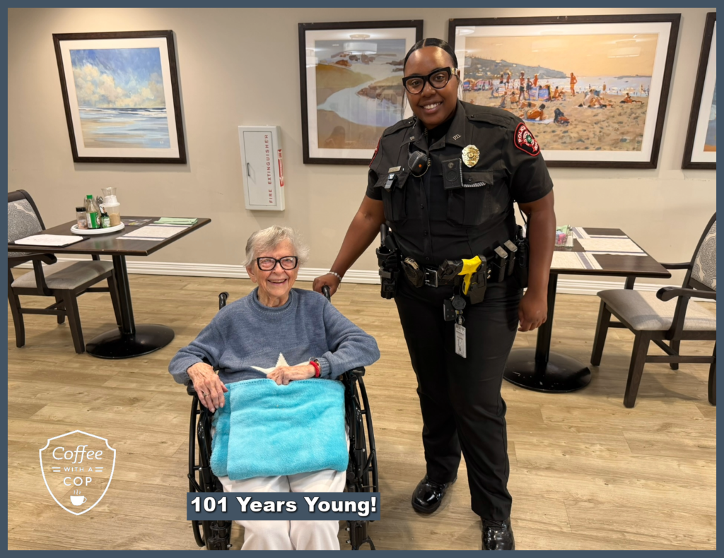 A Meadows Place police officer stands beside a smiling resident in a wheelchair during Coffee with a Cop at The Jasper of Meadows Place. The photo includes the message "101 Years Young!"