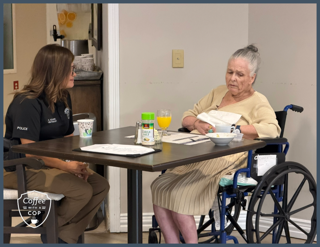 Meadows Place Police Lieutenant Adames sits across from a resident in a wheelchair during Coffee with a Cop. The two share a conversation at a dining table.