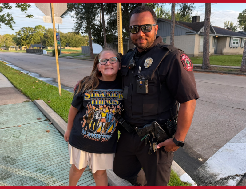 Meadows Place police officer poses with a smiling student near a neighborhood crosswalk.