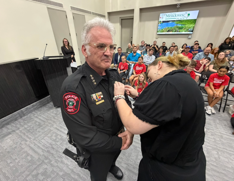Police Chief Jack Ashton’s daughter pins his badge during his swearing in ceremony as family, friends, officers, and community members look on.