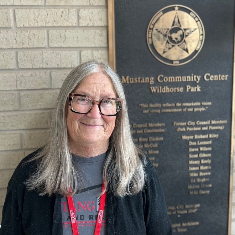 a photo of Ginger Williams standing in front of a Wild Horse Park Plaque