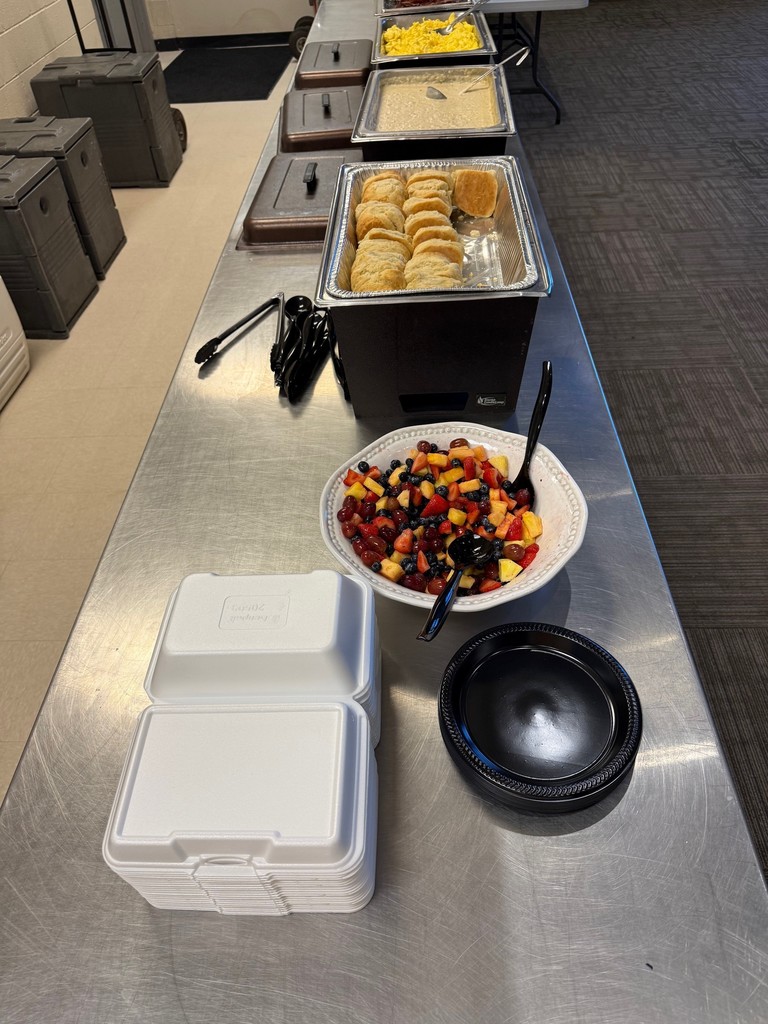 Food in a buffet line with colorful fruit, biscuits, gravy, eggs, and bacon