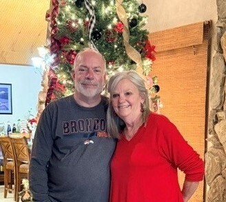 A photo of Lauri Diment with her husband Rick in front of a well decorated Christmas Tree.