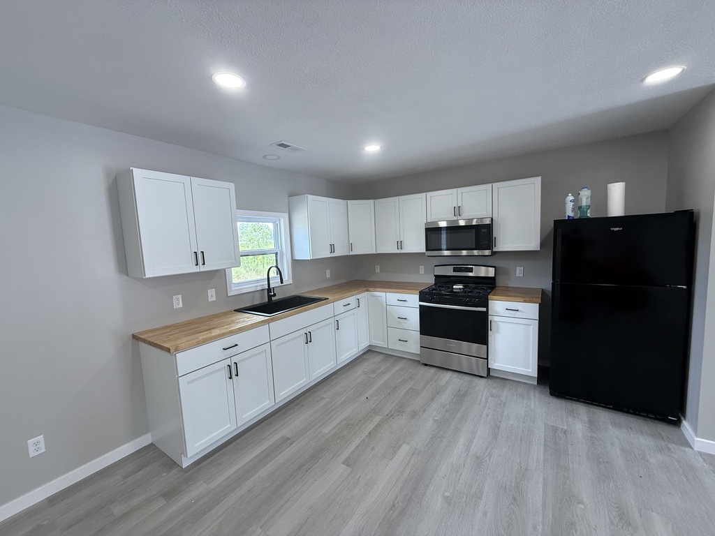 image of a kitchen with grey walls, white cabinets, light wood countertops and a black fridge