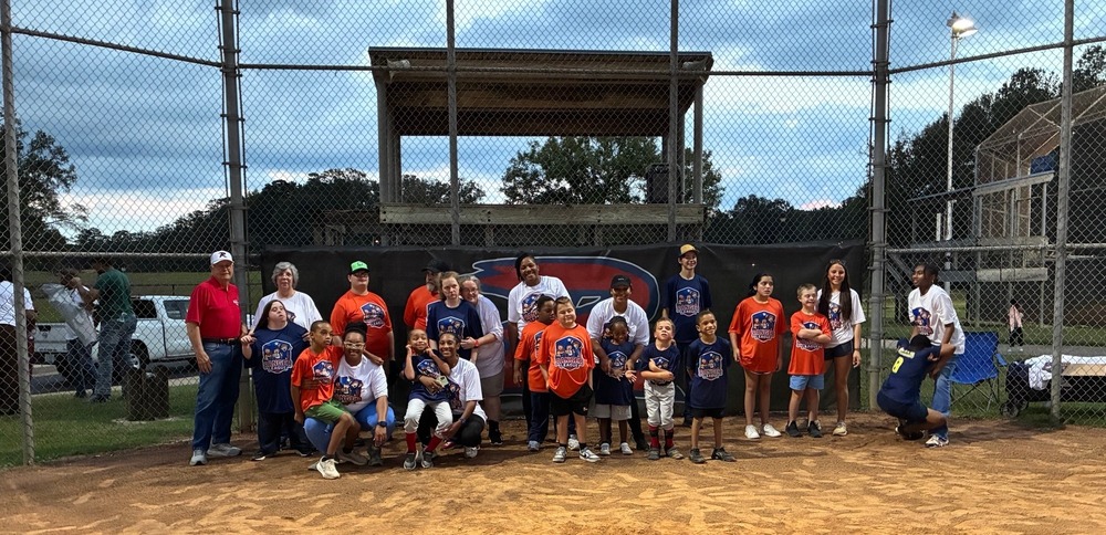 Group photo of Ranger League players, coaches, volunteers, and supporters gathered on the baseball field at Eastside Park following the first game of the season. Participants are wearing Ranger League shirts and posing together in front of the dugout and field.