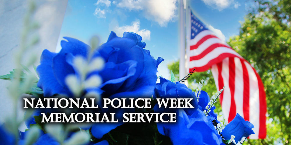 National Police Week Memorial Service - American flag blowing in the breeze with blue flowers in the foreground