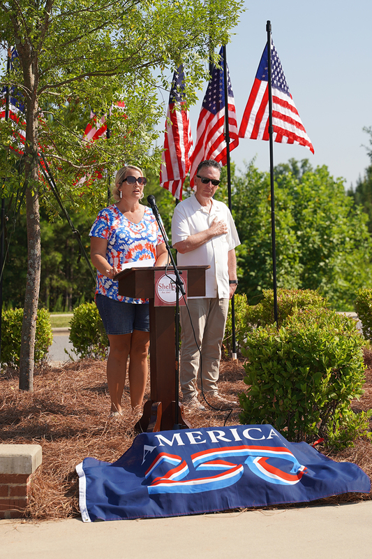 Katie Turner singing the national anthem as the Mayor stands with his hand over his heart