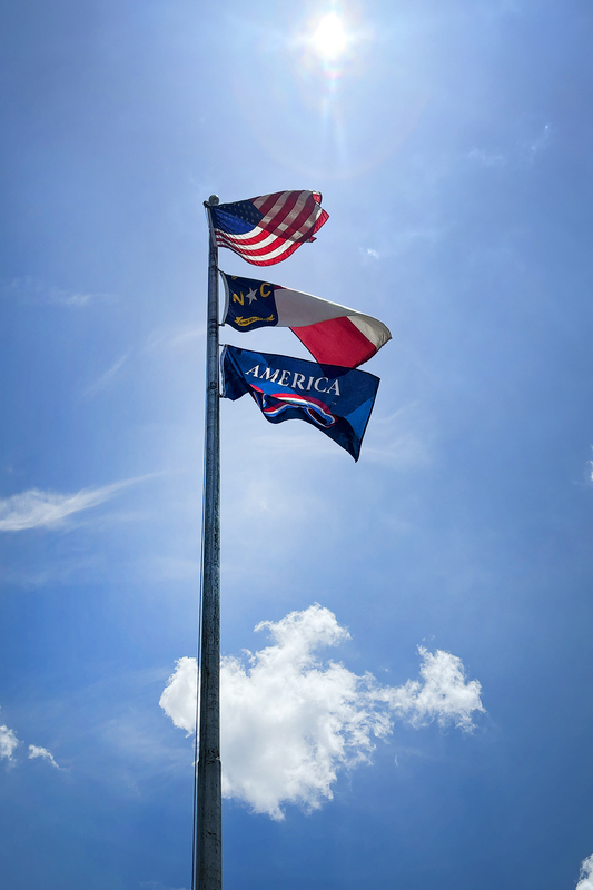 American flag, NC flag, and America 250 flag blowing in the breeze