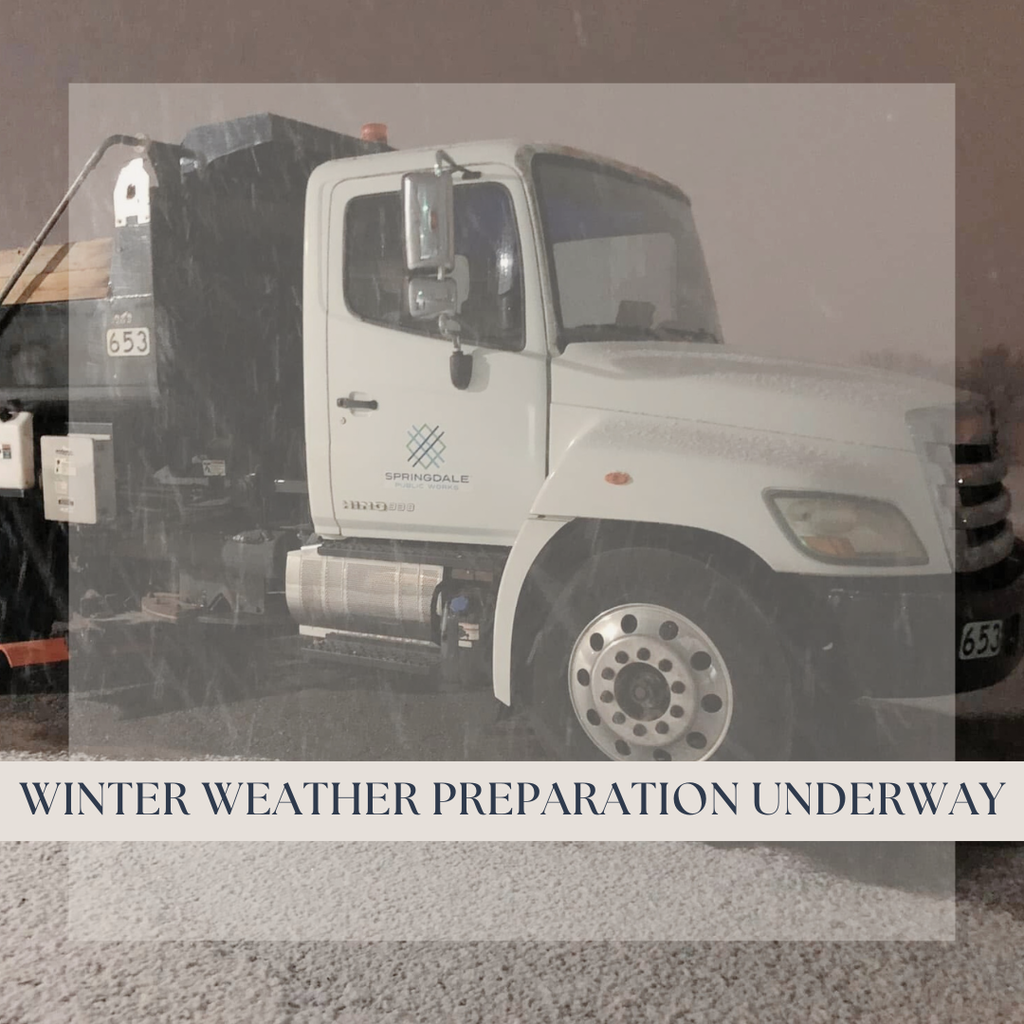 A Springdale Public Works snowplow truck is parked at night during active snowfall, with snow visible on the ground and falling through the air. The white truck displays the Springdale Public Works logo on the door, and a banner across the image reads āWinter Weather Preparation Underway.ā