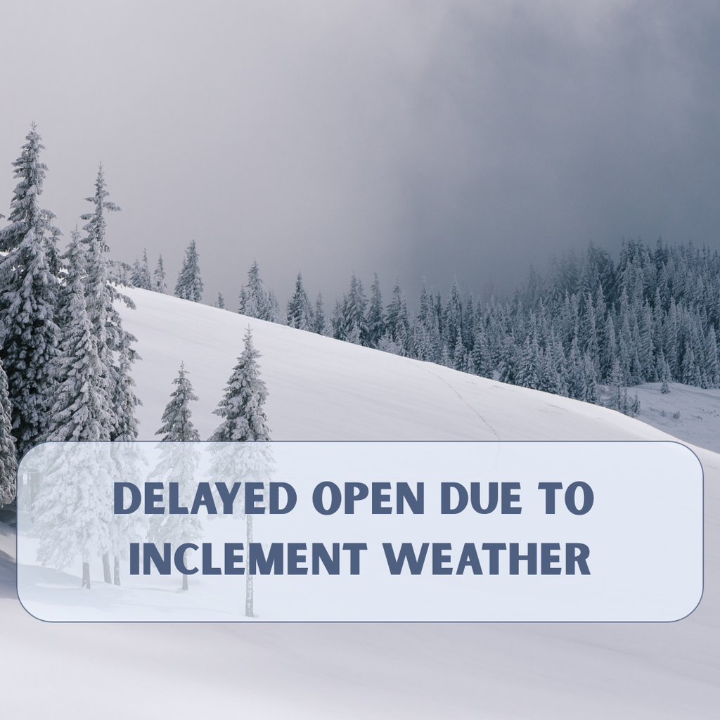 A winter landscape with snow-covered hills and evergreen trees under a cloudy gray sky. Over the lower portion of the image is a semi-transparent blue banner with bold text that reads, āDelayed Open Due to Inclement Weather.ā