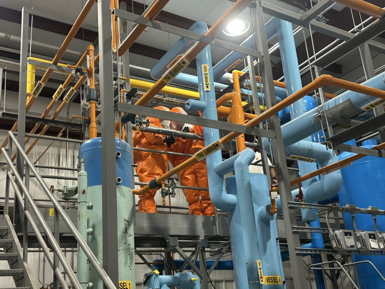 two firefighters in hazmat suits working on a pipe to fix a leak