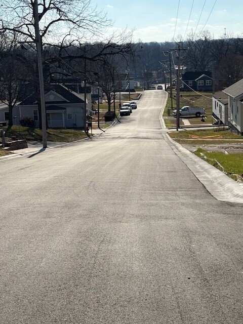 Newly paved street with houses along each side and some cars parked on street