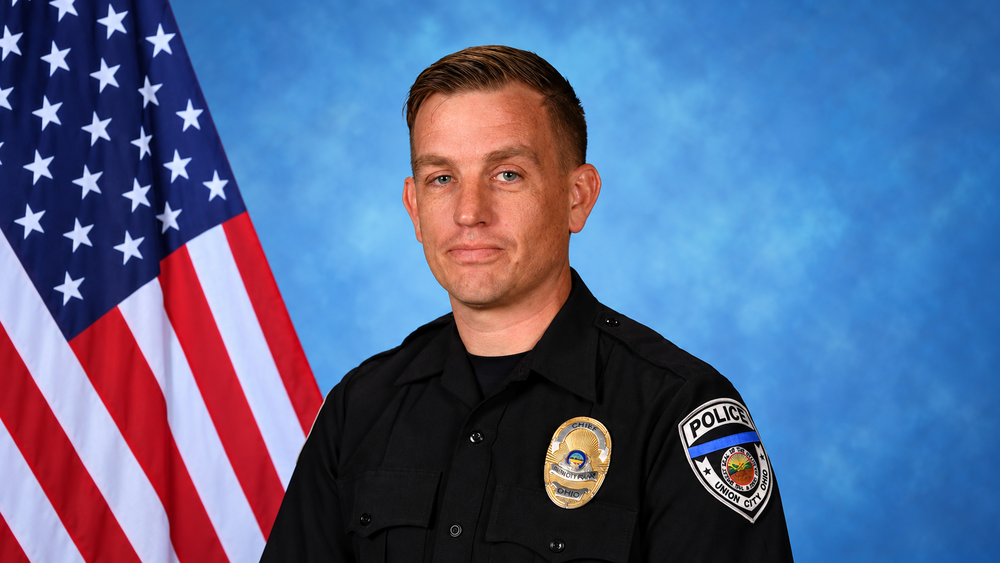 Mark Ater in police uniform seated in front of American flag.