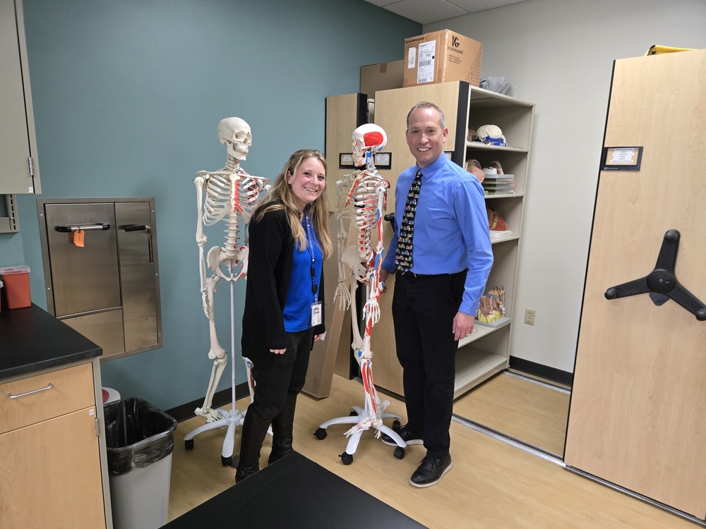 Chelsey Bauer and Mayor Stocks standing in a classroom, next to two skeletons