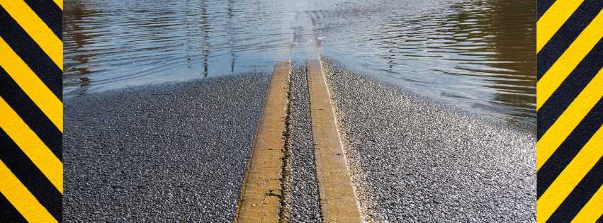 Close-up of flooded roadway , bordered by black and yellow diagonal bars