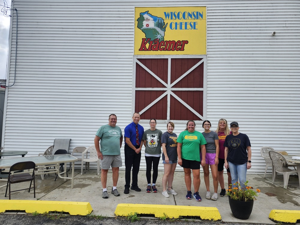 gROUP OF PEOPLE STANDING IN FRONT OF WHITE kRAMER cHEESE BARN