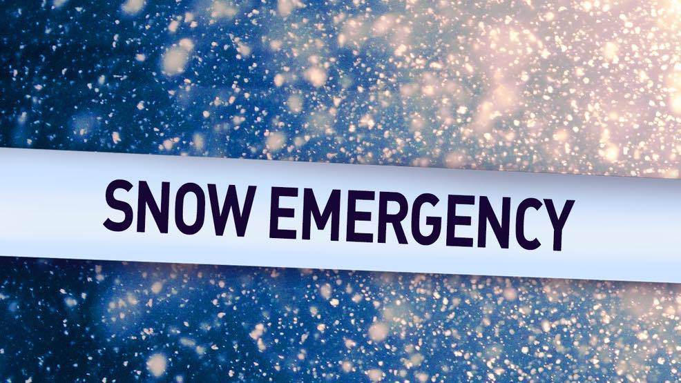 Snow flurries against a dark background, with a white banner containing the words "snow emergency" on it. 