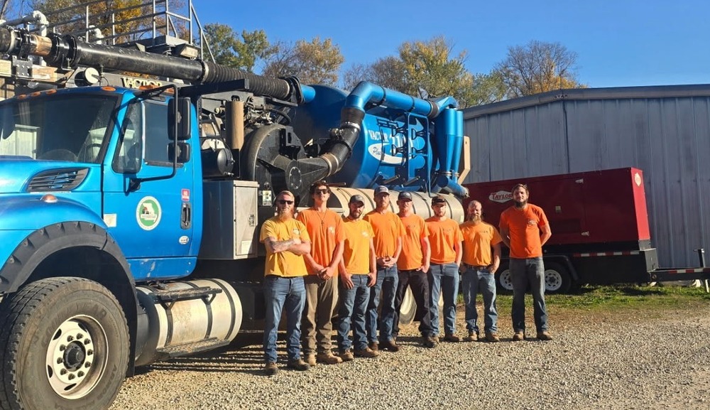 8 City of Waynesville employees standing infront of a blue vactor truck, outdoors with grass on the ground and blue skies.