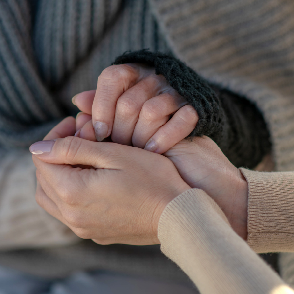 Two people wearing sweaters hold hands to comfort each other.