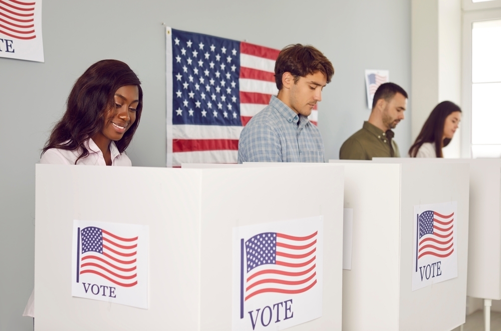 Four people voting in pop-up voting booths branded with the American flag