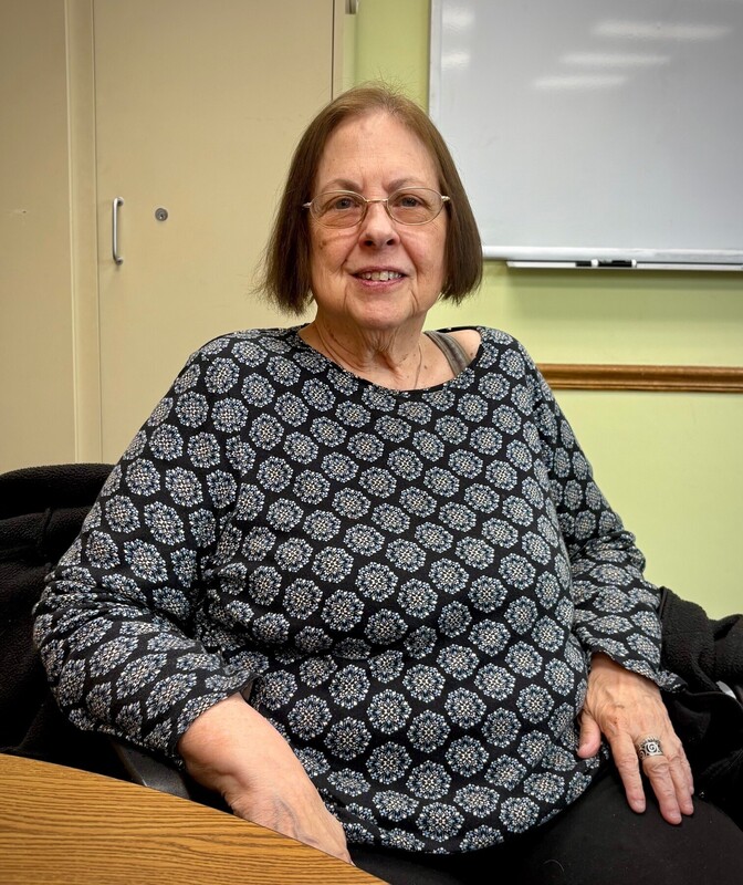 Woman with brown hair sitting in chair with black and white shirt on smiling.