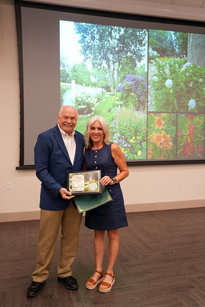 A Westlake in Bloom winner holds her award certificate beside the Mayor, with a collage of her flower garden projected on the screen behind them.