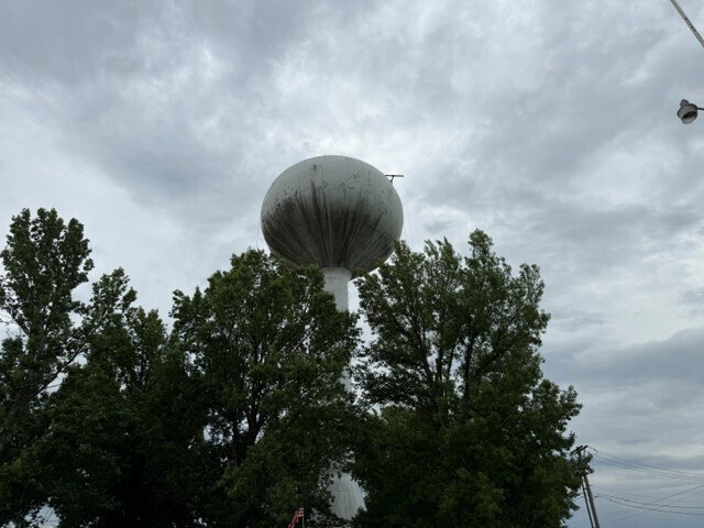 A view of the top of the water tower hidden partially by trees showing more work lines hanging