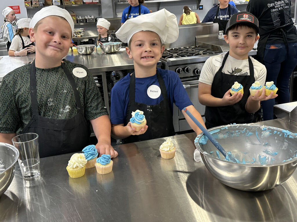 Three young boys participating in the Culinary Arts Camp program making and decorating cupcakes.