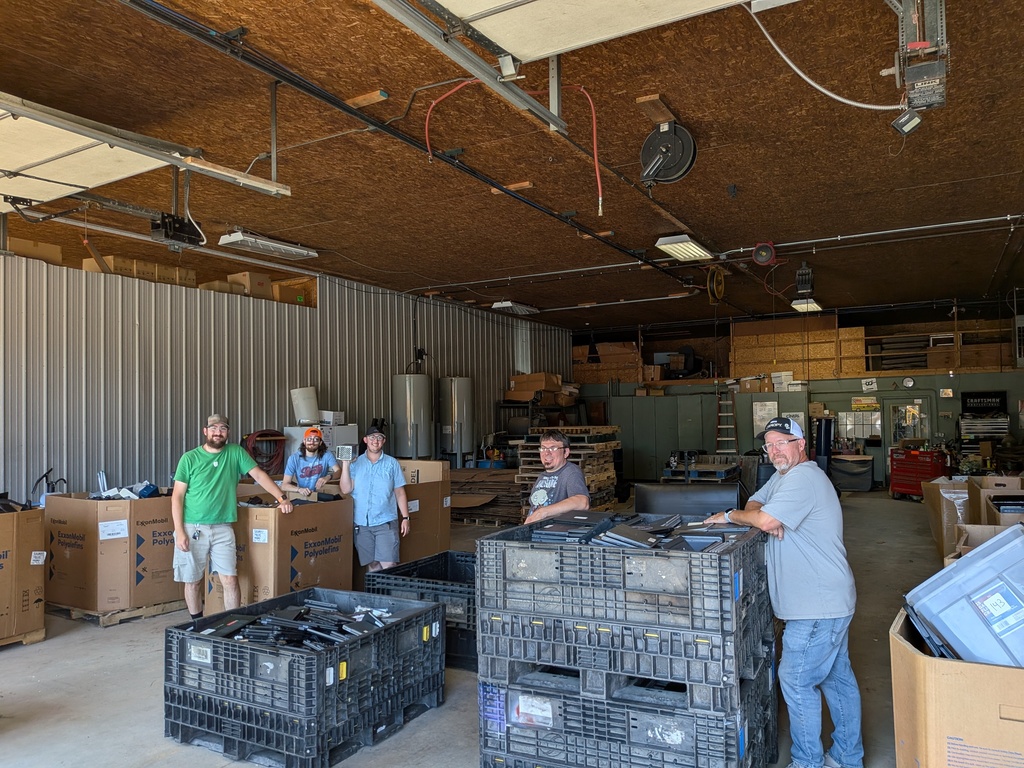 Tech Staff members stand around pallets of scrap electronic waste for recycling.