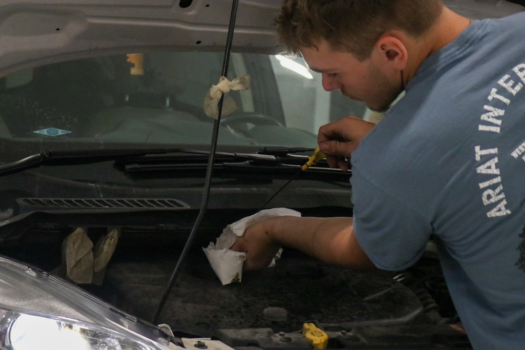 Student checking oil in a car